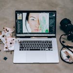 A stylish photography setup with a laptop editing a portrait and a camera surrounded by SD cards on a concrete surface.